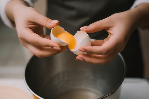 Femme cuisinier dans un tablier gris casse un œuf dans un bol en métal. Séparez la protéine du jaune