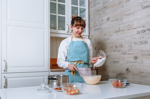 La femme cuisinière ajoute de la farine à la pâte. Le processus de mélange des ingrédients du gâteau dans la cuisine à domicile