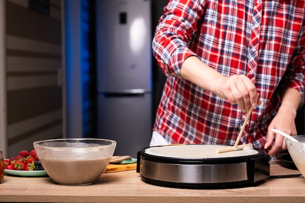 Une femme cuit une délicieuse crêpe sur une machine à crêpes électrique en gros plan dans la cuisine