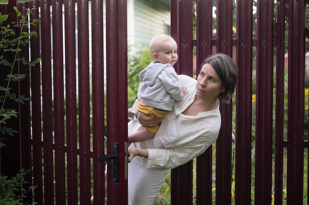Une femme curieuse avec un bébé jette un coup d'œil à la porte de la clôture