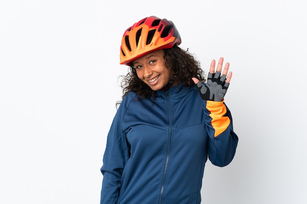 Femme cycliste adolescent isolé sur mur blanc saluant avec la main avec une expression heureuse