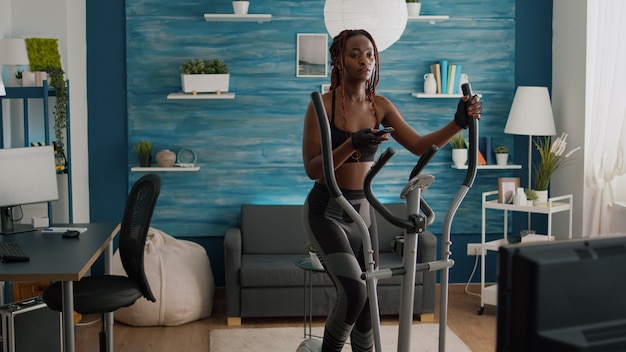 Photo femme cycliste à la peau noire dans le muscle du corps d'entraînement de vêtements de sport à l'aide d'un vélo elliptique