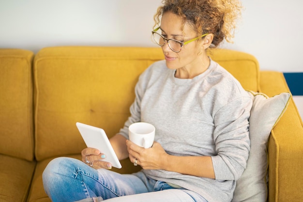 Femme dans l'activité de détente de loisirs à l'intérieur seule lire et utiliser une tablette électronique ereader pour lire un nouvel ebook de la bibliothèque en ligne Personnes et connexion sans fil à la maison Détendez-vous style de vie féminin