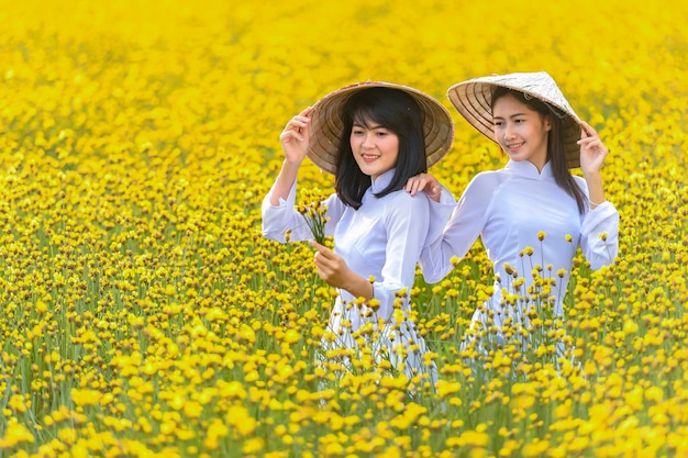 Une femme dans un ancien costume national vietnamien était debout tenant un chapeau en osier parmi les fleurs jaunes