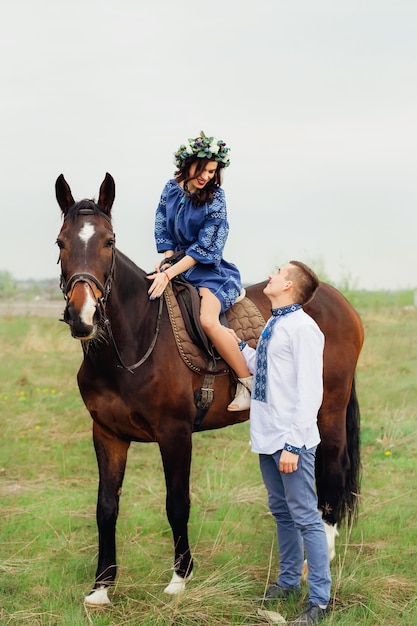 femme dans une belle robe et une couronne sur sa tête est assise sur un cheval et regarde la bien-aimée qui se tient à côté d'elle