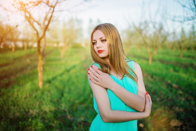 Femme dans une belle robe longue turquoise posant sur un pré dans le jardin.