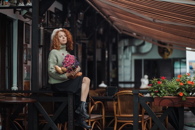 Une femme dans un béret et un pull vert tient un bouquet de fleurs sur un fond de restaurant