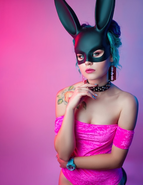 La femme dans un body rose vif et un masque de lapin pose sur un fond clair