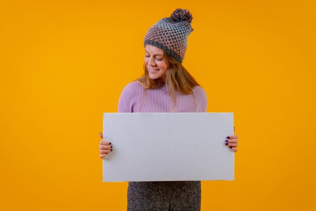 Femme dans un bonnet de laine tenant un panneau d'affichage blanc sur une publicité de fond jaune