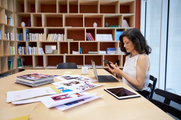 Femme dans un bureau de médias créatifs à l'aide d'un smartphone à son bureau