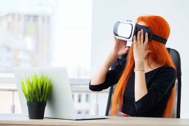Femme dans un casque de réalité virtuelle pointant dans l'air alors qu'il était sur son lieu de travail au bureau.