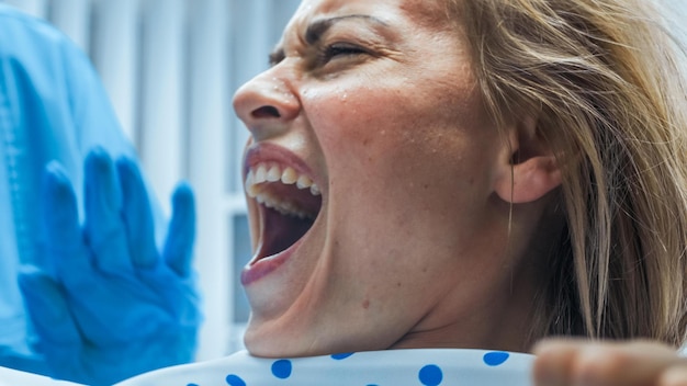 Une femme dans une chaise de dentiste rit et porte des gants bleus.