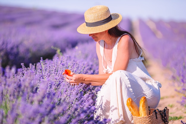 Femme dans le champ de fleurs de lavande au coucher du soleil en robe blanche et chapeau