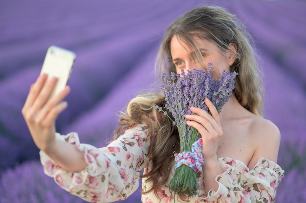 Femme dans un champ de lavande au coucher du soleil prenant selfie