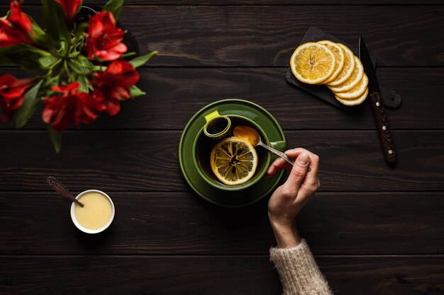 Femme dans un chandail beige confortable buvant une grande tasse de thé chaud avec du citron et du miel sur fond de bois