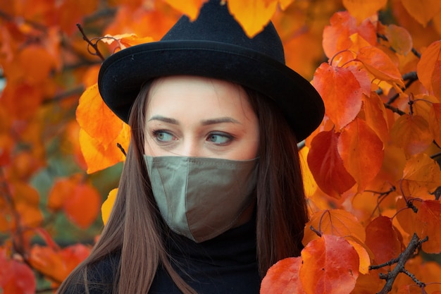 femme dans un chapeau et un masque sur un arbre automne