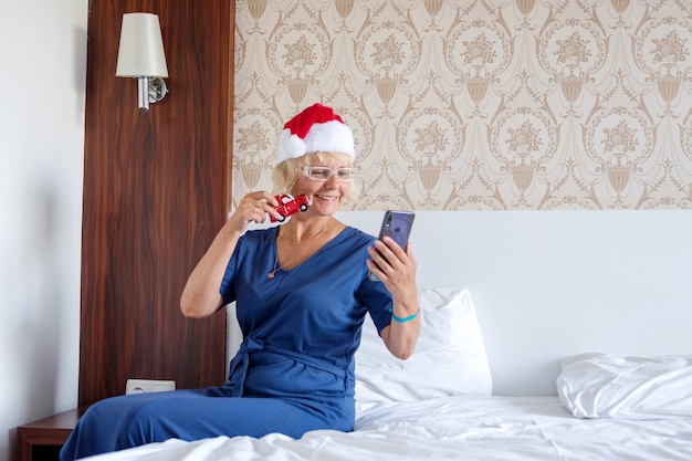 femme dans un chapeau de père Noël avec un smartphone sur le lit