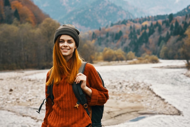 Femme dans un chapeau pull avec un sac à dos reposant près de la rivière dans les montagnes sur le paysage naturel