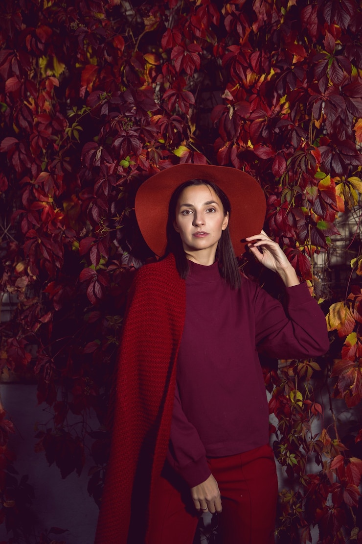 Photo femme dans un chapeau rouge et pull rouge se dresse sur un fond de feuilles d'orange mur de raisins automne