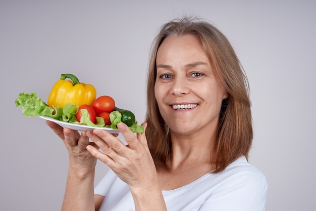 femme dans une chemise blanche tient une assiette avec différents légumes