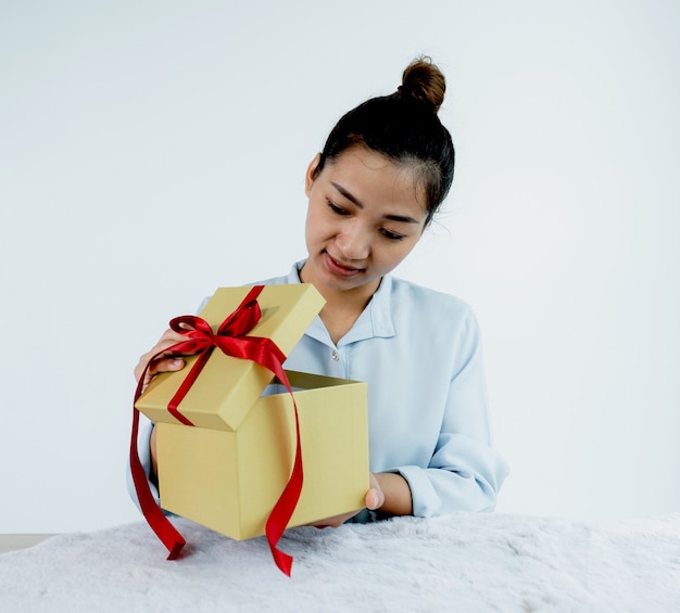 Photo femme dans une chemise bleue ouvrant une boîte cadeau en or attachée avec un ruban rouge présent pour le festival de donner des vacances spéciales comme noël, la saint-valentin.