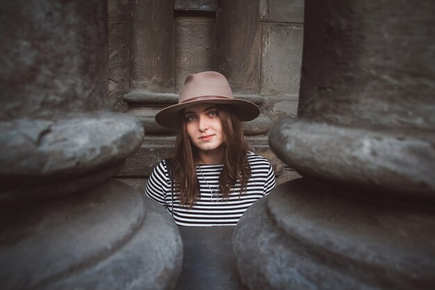 femme dans une chemise rayée tenant son chapeau et regardant une caméra