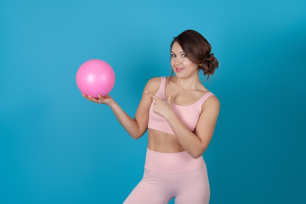 Femme dans un costume rose de Pilates tient une balle et la pointe avec son index