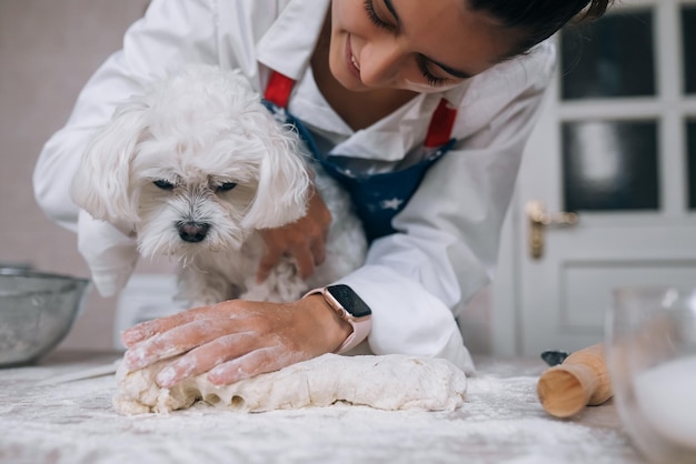 La femme dans la cuisine pétrit la pâte avec son chien