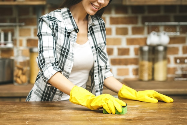 Femme dans la cuisine sourit et essuie la poussière à l'aide d'un spray et d'un plumeau tout en nettoyant sa maison, gros plan