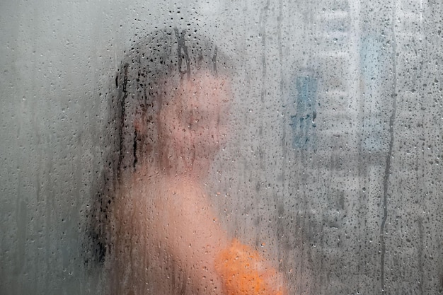 Femme dans la douche vue à travers le verre recouvert de gouttes