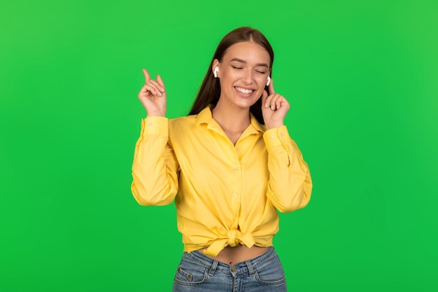 Femme dans les écouteurs écoutant de la musique avec les yeux fermés fond vert