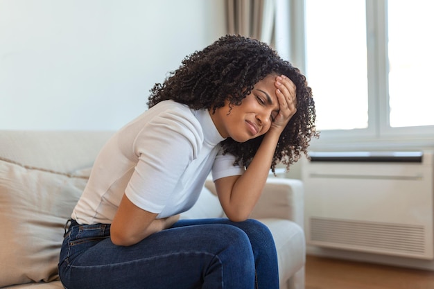 Femme dans une expression douloureuse tenant la main contre le ventre souffrant de douleurs menstruelles couché triste sur le lit à la maison ayant une crampe abdominale dans le concept de santé féminine