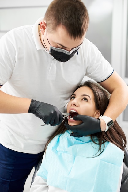 Femme dans le fauteuil dentaire et le dentiste pince sa dent avec une pince en clinique