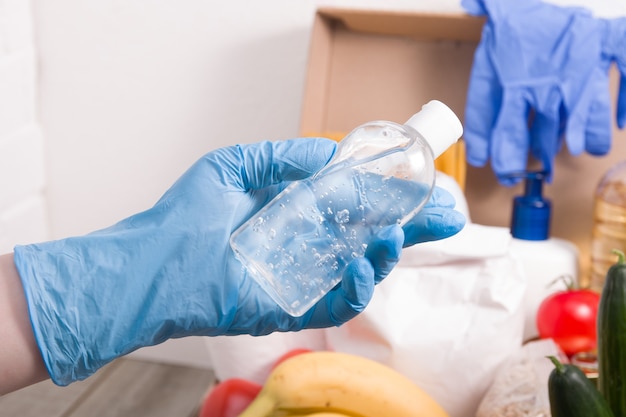 Une femme dans un gant en caoutchouc met un gel désinfectant dans une boîte avec des produits alimentaires et d'hygiène pour un don