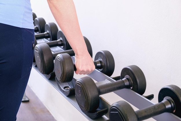 La femme dans le gymnase prend un haltère du support