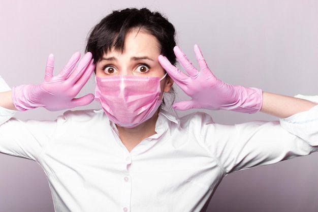 femme dans l'horreur dans une chemise blanche masque médical rose et gants sur fond gris