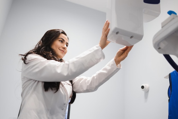 La femme dans un manteau médical ajuste un tomographe dentaire