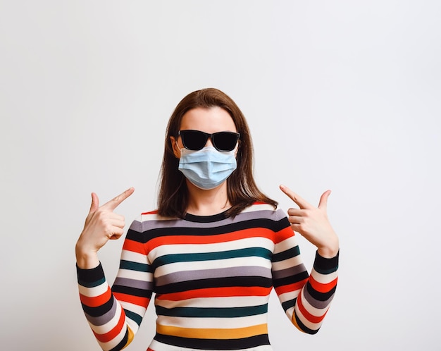 Femme dans un masque médical bleu et des lunettes de soleil noires sur fond clair