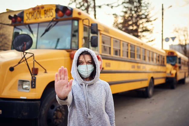 Une femme dans un masque de protection se tient devant un autobus scolaire.