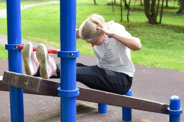 femme dans le parc est engagée dans la gymnastique fille sur barre horizontale gymnastique à l'extérieur