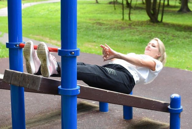 femme dans le parc est engagée dans la gymnastique fille sur barre horizontale gymnastique à l'extérieur