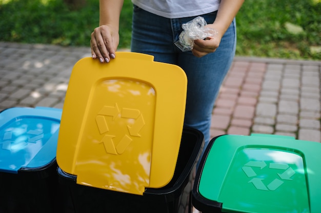 Femme dans le parc jetant un sac en plastique dans un bac de recyclage de différentes couleurs sur des bacs en plastique vert