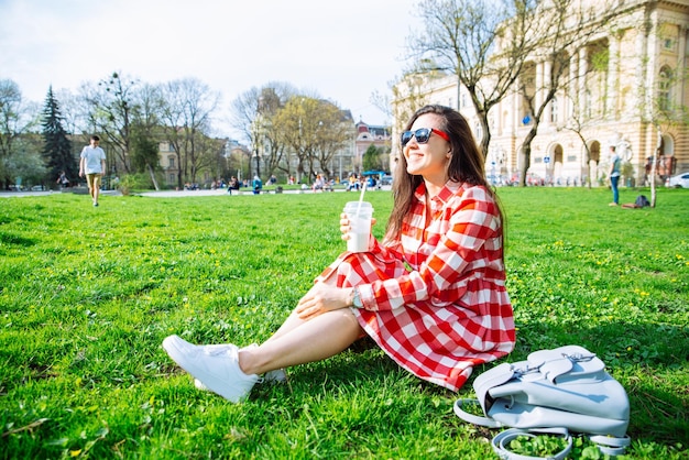 Femme dans le parc de la ville assise sur le sol et buvant un smoothie