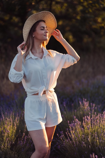 Une femme dans un pré de lavande se tient en chemise blanche et un short et est éclairée par les rayons du soleil pendant