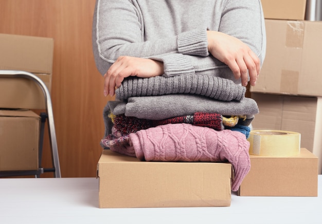 Femme dans un pull gris emballant des vêtements dans une boîte, le concept d'assistance et de bénévolat, en mouvement. Vendre des choses inutiles
