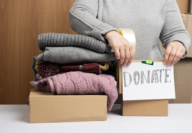 Femme dans un pull gris est l'emballage des vêtements dans une boîte, le concept d'assistance et de bénévolat, de don