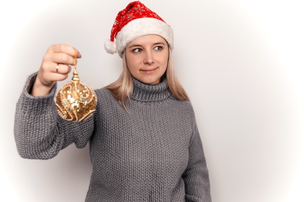 une femme dans un pull en laine gris et un bonnet de noel tient des décorations de noël dans ses mains