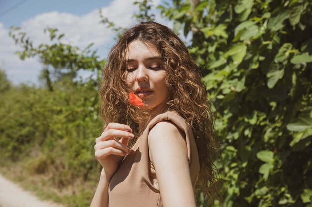 femme dans une robe beige sentant une fleur de pavot