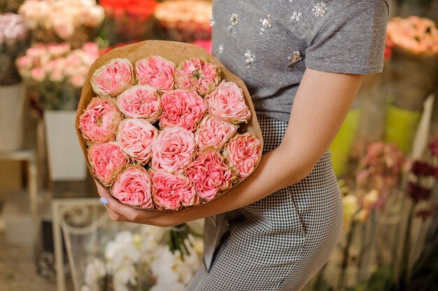 Femme dans une robe grise tenant un bouquet de fleurs rose