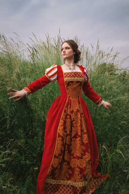 Femme dans une robe médiévale rouge debout dans l'herbe